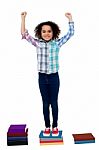 Excited Pretty School Child Standing On Books Stock Photo