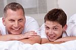 Friendly Father And Son Smiling And Lying On The Bed Stock Photo