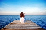 Girl Sitting Alone And Hand Holding Camera On A The Wooden Bridge On The Sea Stock Photo