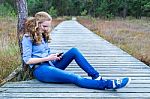 Girl Sitting On Wooden Path In Nature Phoning Mobile Stock Photo
