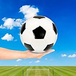 Hand Holding Soccer Ball With Soccer Field And Blue Sky Stock Photo