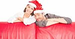 Happy Couple Wearing Santa Hats Behind Red Sofa Stock Photo