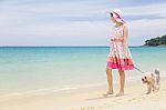 Happy Little Girl In Pink Dress With Her Small Dog Or Puppy Walking Together On Beautiful Beach Stock Photo