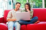Happy Young Couple Using Laptop On Red Sofa Stock Photo