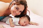 Hispanic Mom Lying Down On Bed And Holding Her Infant Son Stock Photo