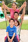 Jolly Caucasian Family Swinging In The Park Stock Photo