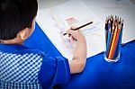 Little Asian Boy Sitting At The Table And Drawing By Colour Pencil Stock Photo