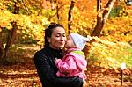 Little Girl Kissing Her Mom On Autumn Background Stock Photo