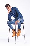 Male Model In Denim Jeans Sitting On A Chair . Studio Shoot Stock Photo