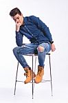 Male Model In Denim Jeans Sitting On A Chair . Studio Shoot Stock Photo