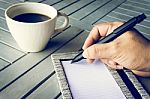 Man Hand With Pen Writing On Notebook. Coffee And Notebook On Wooden Table Stock Photo