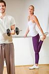 Man Lifting Dumbbell And Woman Stretching In Gym Stock Photo
