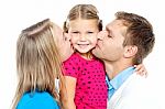 Mom And Dad Kissing Their Beautiful Kid Stock Photo