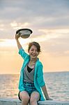 Portrait Of Beautiful And Happy Emotion Teenager Wearing Straw Hat Sitting On Bridge Beside Sea Beach Against Sun Set Sky Stock Photo