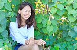 Portrait Of Pretty Woman Sitting In Green Leaves Bush And Smilin Stock Photo
