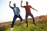 Portrait Of Two Friends Jumping In Field Stock Photo
