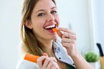 Pretty Young Woman Eating Carrot In The Kitchen Stock Photo