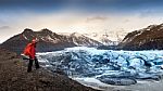 Professional Photographer With Camera And Tripod In Winter. Professional Photographer Looking To Glacier In Iceland Stock Photo