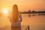 Silhouette Of Relaxing Young Woman On Wooden Pier At The Lake In Sunset Stock Photo