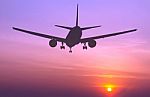 Silhouetted Commercial Airplane Flying At Sunset Stock Photo