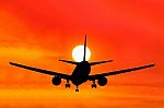 Silhouetted Commercial Airplane Flying At Sunset Stock Photo