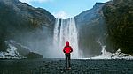 Skogafoss Waterfall In Iceland. Guy In Red Jacket Looks At Skogafoss Waterfall Stock Photo