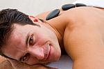 Smiling Young Man Receiving Hot Stone Treatment Stock Photo