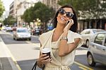 Smiling Young Woman With Coffee Laughs Into Phone On Street Stock Photo