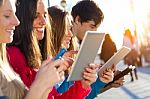 Students Having Fun With Smartphones And Tablets After Class Stock Photo