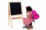 Thoughtful Kid Sitting In Front Of Blackboard Stock Photo