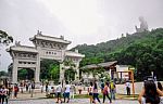 Tourists At The Gate To Po Lin Monastery With Tian Tan Buddha Statue Up On The Hill In Background, Ngong Ping Village, Lantau Island, Hong Kong Stock Photo