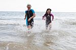 Two Girl Wearing Wet Suit  Playing On Sea Beach With Happiness E Stock Photo