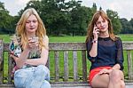 Two Girls On Bench In Park Calling Mobile Stock Photo