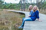 Two Sisters Sitting On Wooden Path In Forest Stock Photo