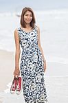 Young Asian Woman With Smiling Face Wearing Long Dress Standing With Sneaker In Hand On Sea Beach Stock Photo