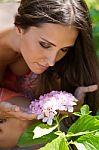 Young Beautiful Girl Smells Flowers, Against Green Summer Garden Stock Photo