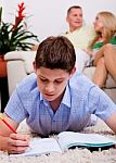 Young Boy Studying With Family In The Background Stock Photo
