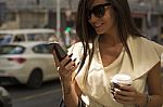 Young Brunette Laughs Into Phone, Hod Coffee In Another Hand Stock Photo