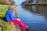 Young Girl Sitting At Waterfront Of Canal Stock Photo