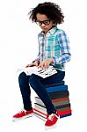 Young Kid Sitting On Stack Of Books And Reading Stock Photo