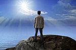 Young Man Standing On Rock Mountain And Looking To The Sun Stock Photo