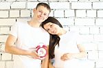Young Pregnant Woman And Her Husband With Red Alarm Clock Stock Photo