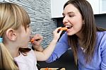 Young Woman And Little Girl Eating Carrots In The Kitchen Stock Photo