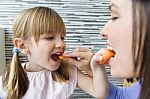 Young Woman And Little Girl Eating Carrots In The Kitchen Stock Photo