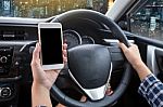 Young Woman Driver Using Touch Screen Smartphone And Hand Holding Steering Wheel Stock Photo