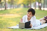 Young Woman Lying On Green Grass Park With Pencil And Note Book Stock Photo
