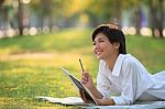 Young Woman Lying On Green Grass Park With Pencil And Note Book Stock Photo