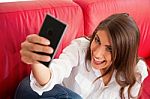 Young Woman Making Face While Taking Selfie On Sofa Stock Photo