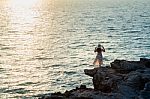 Young Woman Standing On The Top Of Rock And Looking At The Seashore And Sunset In Si Chang Island Stock Photo